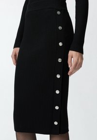 Schwarzer gerippter Strickrock mit körperbetontem Design, versehen mit silbernen Knopfakzenten an einer Seite und einem strukturierten Stoff.