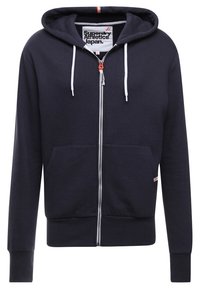 Námořnicky modrá mikina na zip z měkké látky, s kapucí, bílými šňůrkami, předními kapsami a malým logem na boku.