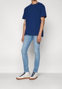 Laivastonsininen puuvillainen t-paita, rento istuvuus; vaaleansiniset kapeat farkut kulunein yksityiskohdin; valkoiset korkeavartiset tennarit laivastonsinisin nauhoin ja vaaleanruskein pohjin.