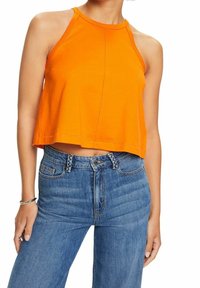Femme portant un haut court orange sans manches associé à un jean bleu taille haute, les mains détendues le long du corps.