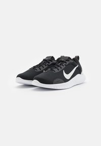 Baskets de sport noires avec une tige en mesh texturé, logo Nike swoosh blanc et semelle en caoutchouc blanche. Comprend des lacets plats et une languette.