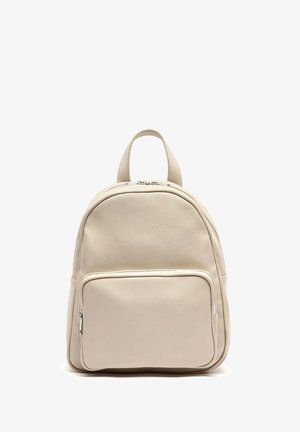 Mochila de cuero beige con forma redondeada, superficie texturizada, un asa superior y un bolsillo con cremallera en la parte frontal. Presenta acentos de hardware en color plateado.