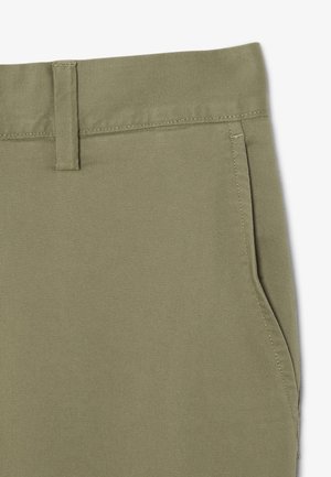 Primer plano de pantalones caqui con un passador para cinturón y bolsillo lateral, mostrando la costura detallada y la textura de la tela.