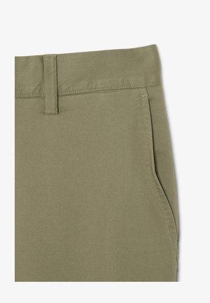 Primo piano di pantaloni color kaki con passante per cintura e tasca laterale, che mostrano cuciture dettagliate e trama del tessuto.