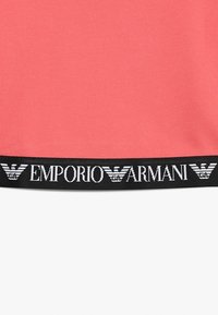 Tela de color coral con banda elástica negra que presenta el logotipo de Emporio Armani y el texto del nombre de marca en la parte inferior.