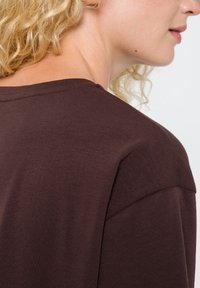 Brązowy bawełniany t-shirt z okrągłym dekoltem i krótkimi rękawami, charakteryzujący się gładką teksturą i subtelnymi szwami na ramieniu.