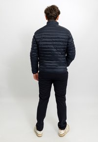 Giubbotto imbottito blu navy con cuciture orizzontali, collo alto e maniche lunghe, abbinato a pantaloni neri e sneaker bianche.