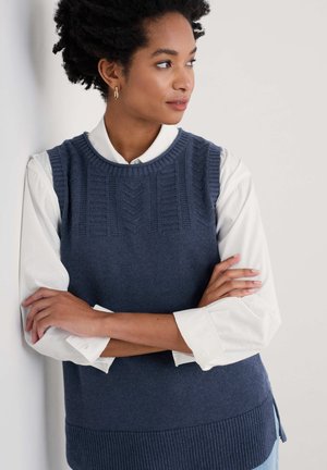 Navy gestrickte Sweaterweste mit einem strukturierten Muster, Rundhalskragen und seitlichen Schlitzen, kombiniert mit einem weißen Hemd mit Kragen.