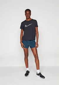Nike svart T-skjorte med hvit logo, blå shorts og svarte løpesko. Har en avslappet passform og fukttransporterende stoff.