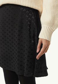 Schwarzer strukturierten Rock mit einem gemusterten Design. Der Stoff wirkt glatt, kombiniert mit einem cremefarbenen Strickpullover.