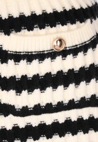 Gestrickter Pullover mit schwarz-weißen horizontalen Streifen, ausgestattet mit einer Tasche und einem glänzenden runden Knopf. Weicher Stoff.