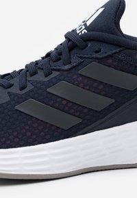 Marinblå Adidas-sneakers med svarta ränder, texturerad mesh-överkant, vadderad krage, snören och vit vadderad sula.