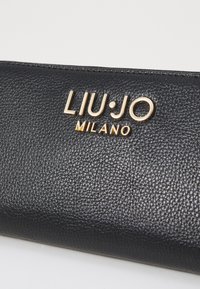 Zwarte leren portemonnee met een prominente gouden logo dat "LIU·JO MILANO" leest. Het oppervlak heeft een korrelige textuur.