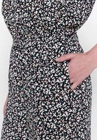 Zwart patroondede jurk met een klein wit bloemmotief, voorzien van kleurrijke accenten, een elastische tailleband en zijzakken. Zachte stoftextuur.