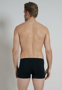 Boxer in cotone neri con elastico in vita, esposti su un torso maschile nudo visto da dietro, che mostrano un design aderente e una superficie liscia.
