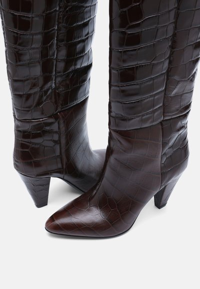 Bottes mi-mollet en cuir marron foncé à motif crocodile, bouts pointus et talons blocs effilés sur fond blanc.