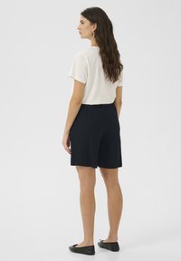 Relaxed-fit cream t-shirt paired with navy elastic-waist shorts. Model wears black flats and has wavy hair styled down. Simple, minimalist design.