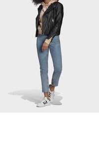 Svart läderbikerjacka, beige hoodie, ljusblå kort denimjeans och vita sneakers med svarta ränder.