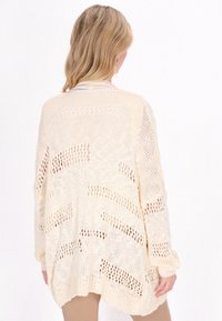 Cardigan crema a maglia aperta con vestibilità morbida, caratterizzato da motivi a zigzag e polsini a coste. Tessuto morbido e maniche lunghe.