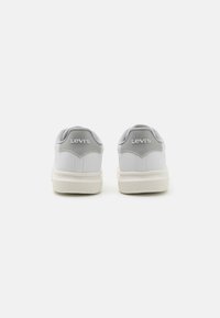 Białe skórzane sneakersy z szarymi akcentami, z wyściełanymi kołnierzami, teksturowanym językiem, grubymi podeszwami i wyraźnym logo na pięcie.