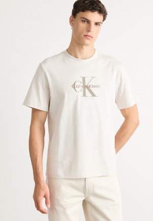 Lichtbeige katoenen T-shirt met korte mouwen, voorzien van een grote bruine Calvin Klein-logo-opdruk aan de voorkant en een ronde hals.