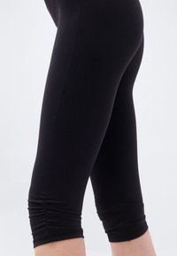 Μαύρο κάπρι κολάν από ελαστικό ύφασμα με λεία υφή, με πιέτες στο τελείωμα και κομψό σχέδιο.