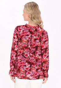 Langärmlige Bluse mit einem Blumenmuster in den Farben Rot, Pink und Lila. Leichter Stoff mit einem gerafften Ausschnitt und Bündchen.