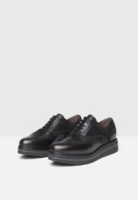 Scarpe in pelle nera con una finitura liscia e testurizzata, design con lacci e una suola robusta e massiccia.