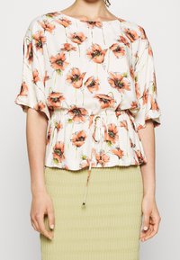 Kwiatowa bluzka w jasnej kremowej kolorze z pomarańczowym wzorem maków, z krótkimi rękawami, dopasowaną talią ze sznurkiem i luźnym krojem.