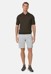 Ciemnobrązowa krótka koszulka polo z kołnierzykiem, zestawiona z jasnoszarymi szortami i szarymi butami sportowymi, tworząca casualowy strój.