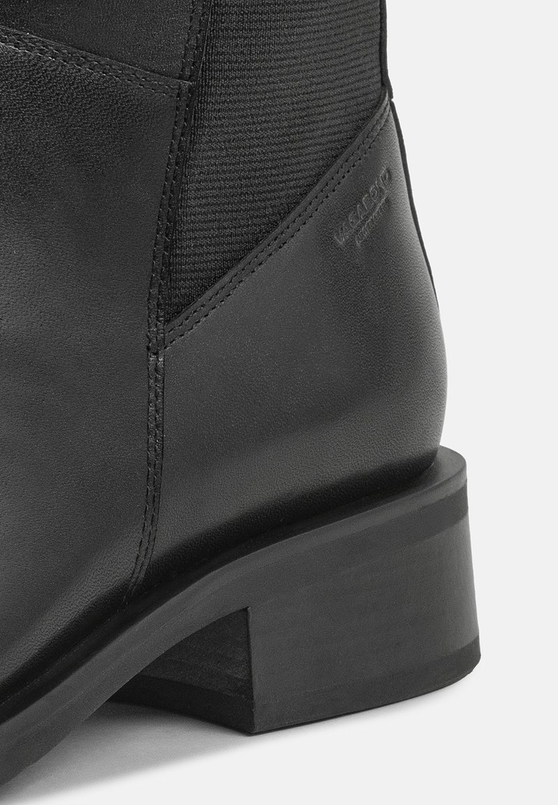 Stivale alla caviglia in pelle nera con pannello in tessuto texture, punta squadrata e tacco spesso. Presenta dettagli con logo distintivo sul lato.