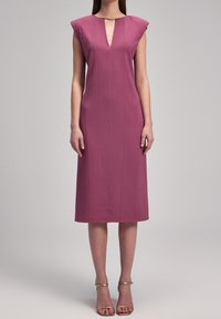 Robe ajustée à manches courtes en forme de casquette, de couleur mauve foncé, longueur genou avec un décolleté en V et des coutures verticales discrètes ; associée à des sandales dorées à lanières.