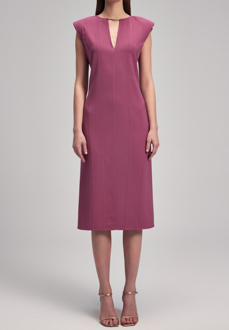 Robe ajustée à manches courtes en forme de casquette, de couleur mauve foncé, longueur genou avec un décolleté en V et des coutures verticales discrètes ; associée à des sandales dorées à lanières.