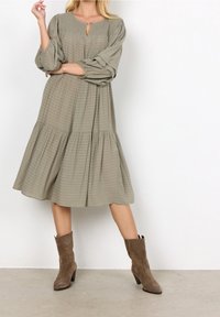 Olijfgroen, jurk tot halverwege de benen met lange pofmouwen, gemêleerde strepen en een keyhole detail aan de voorkant. Gecombineerd met bruine suède enkellaarsjes.
