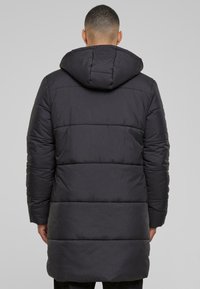 Crna pufasta jakna s kapuljačom, s posutom dizajnom, dužeg kroja i elastičnim manžetama. Glatka tekstura i minimalni detalji.