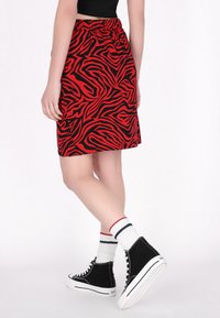 Fustă cu imprimeu de zebra în roșu și negru, cu talie elastică, purtată împreună cu adidași negri cu guler înalt și ciorapi albi cu dungi colorate.
