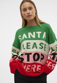 Groene gebreide trui met een oversized pasvorm, voorzien van grote tekst in contrasterende kleuren: "SANTA PLEASE STOP HERE" met rode manchetten en zoom.