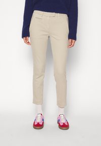 Beige Baumwollhosen mit schmaler Passform, vorderen Taschen und gekrempelten Säumen, kombiniert mit bunten Sneakers, die pinke, blaue und rote Akzente aufweisen.