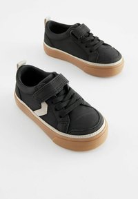 Svarta sneakers med en texturerad läderöverdel, kontrasterande beige detaljer, ett kardborreband och en gummisula i brunt.
