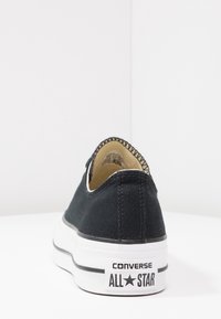 Baskets en toile noire avec une semelle en caoutchouc blanche. Présentent une surpiqûre noire et un onglet de talon marqué avec l'inscription « CONVERSE ALL STAR ».