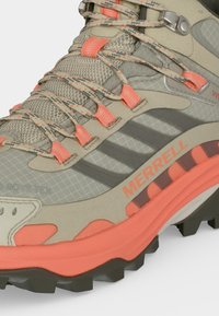Gros plan d'une chaussure de randonnée Merrell beige et corail avec des lacets texturés, une tige en mesh et une semelle extérieure noire robuste.