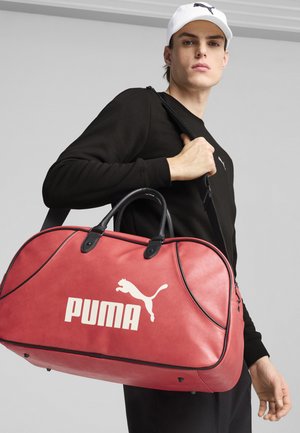 Borsa a viaggio in pelle rossa con dettagli neri, forma arrotondata e logo Puma bianco. Presenta manici doppi e una tracolla staccabile.