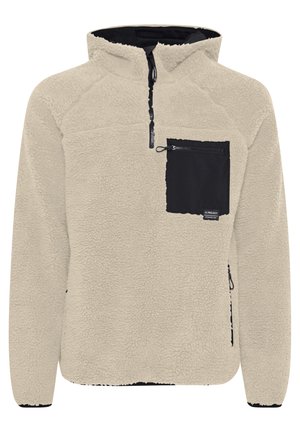 Beige fleece pullover met een zwarte borstzak. Heeft een ritssluiting en een textuurstof. Gebreid ontwerp met contrasterende details.