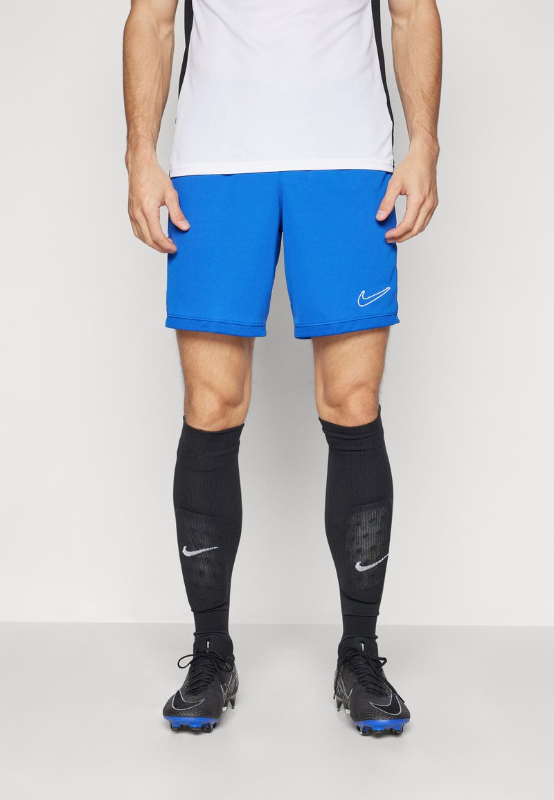 Blauwe sportshorts met wit Nike-logo, gecombineerd met zwarte kniekousen met gestructureerde accenten en zwarte voetbalschoenen.