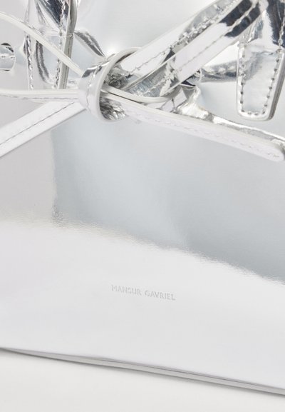 Silver metallic handbag featuring a glossy finish, patterned straps, and a small embossed logo at the bottom.