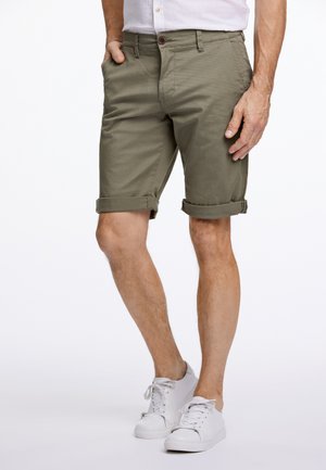 Olijfgroene shorts van lichtgewicht stof, met een omgeslagen zoom en zijzakken, gecombineerd met witte sneakers.