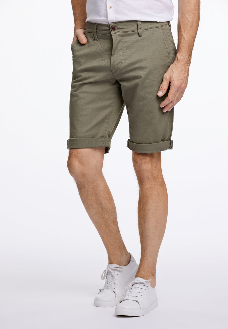 Olivgröna shorts i lätt tyg, med vikta fållar och sidfickor, kombinerat med vita sneakers.