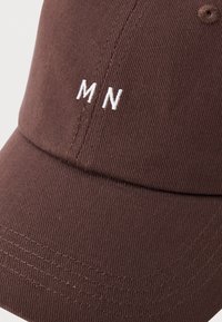 Brun keps med en strukturerad design, tillverkad av bomull, synliga sömmar och vit "MN" broderi på framsidan.