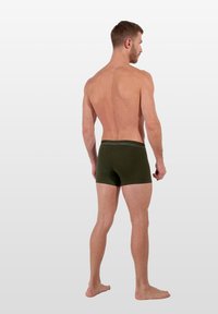 Boxers de algodón verde oliva con un corte ajustado y cintura elástica, mostrados desde la parte trasera sobre un torso desnudo. Textura suave, diseño minimalista.
