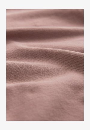 Tissu rose doux avec une texture de tricot fin visible et des plis délicats créant des ombres subtiles sur la surface.